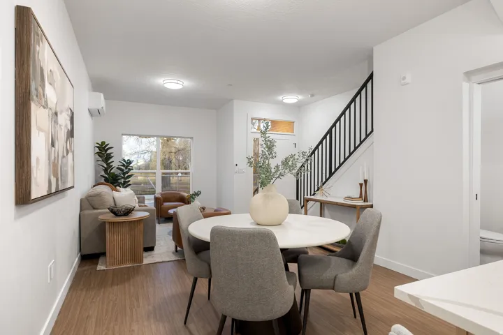 Open-concept living and dining area with wood-finish flooring, a white round dining table, and a contemporary black metal staircase railing