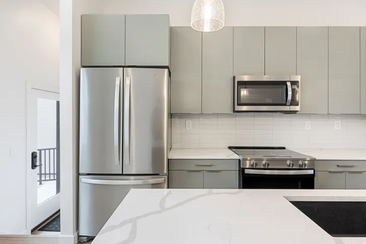 Stainless steel appliances, light-toned cabinetry, subway tile backsplash, quartz countertops, and a modern pendant light fixture