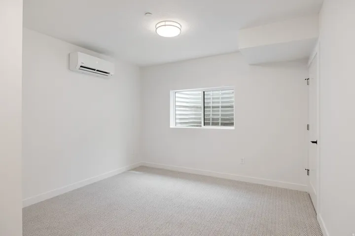 Recessed lighting, wall-mounted air conditioning unit, white trim, textured carpet, and a window with a glass block exterior