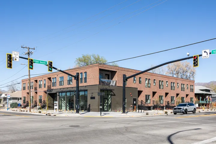 Corner building featuring brick siding, large storefront windows, multiple balconies, and dark-framed windows
