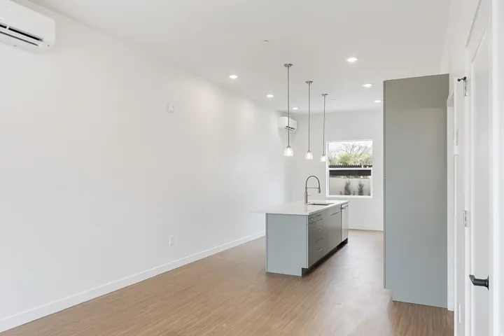 Kitchen island with an undermount sink and gooseneck faucet, light wood-finish flooring, recessed lighting, and pendant lighting