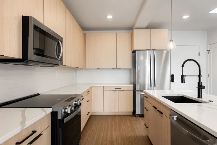 Kitchen featuring light wood-finish cabinetry, white countertops, stainless steel appliances, and a tile backsplash