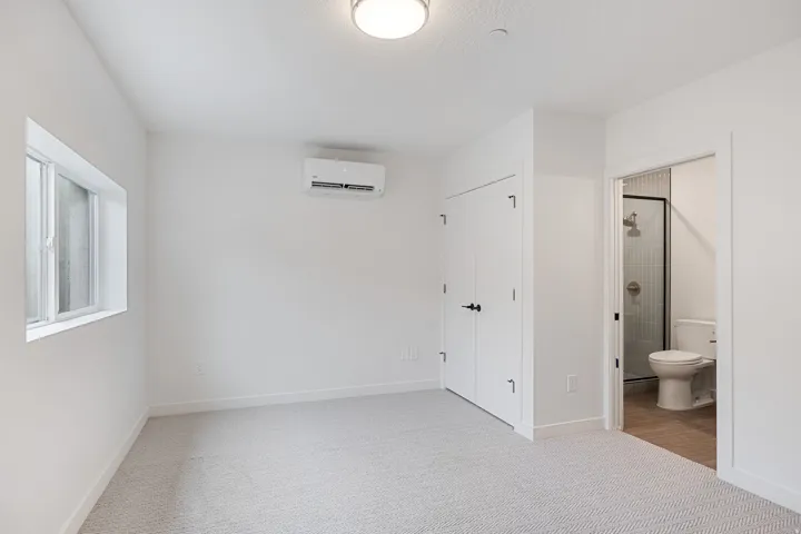 Recessed ceiling lighting, wall-mounted air conditioning unit, white interior doors, window with white trim, and light-colored patterned carpet