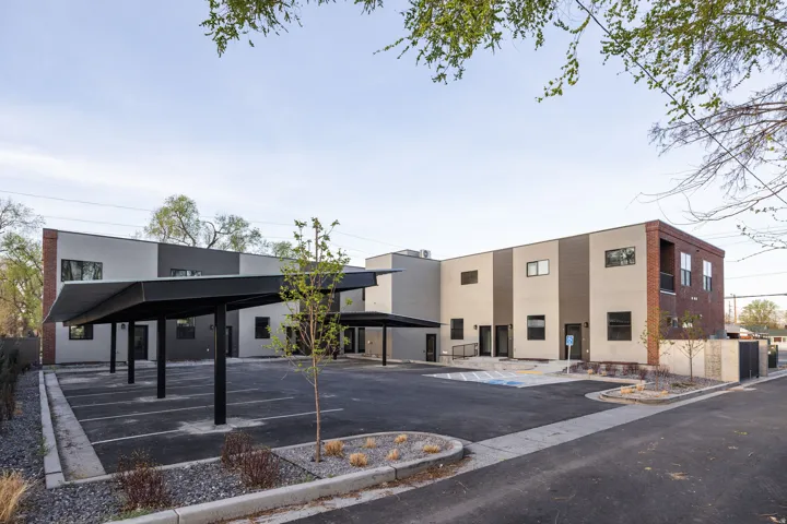 Multi-unit property featuring contemporary architecture with brick accents, covered parking, a paved parking lot, and a designated accessible parking space