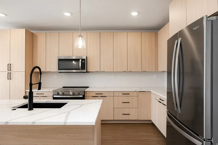 Kitchen featuring wood-finish cabinetry, stainless steel appliances, a black sink with a matte black faucet, and white countertops with veining