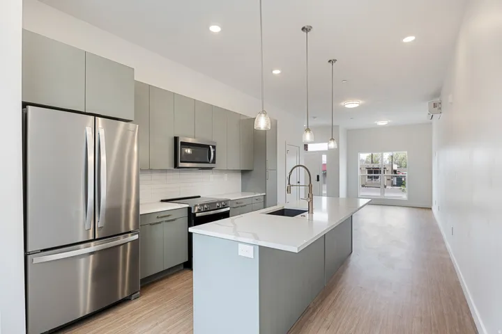Modern kitchen featuring stainless steel appliances, light-toned cabinetry, a spacious island with an integrated sink, pendant lighting, and wood-finish flooring