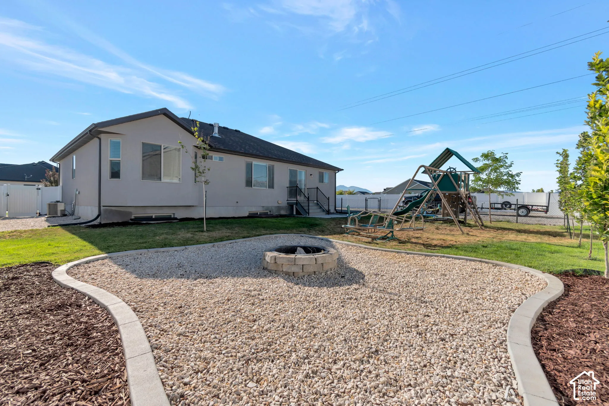 Expansive backyard featuring a gravel fire pit area with paver edging, wood chip landscaping, and a manicured lawn