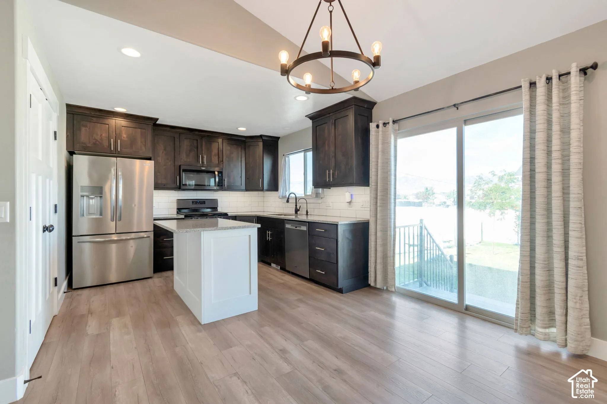 Kitchen featuring wood-finish flooring, dark wood cabinetry, white subway tile backsplash, and a central island with a white base