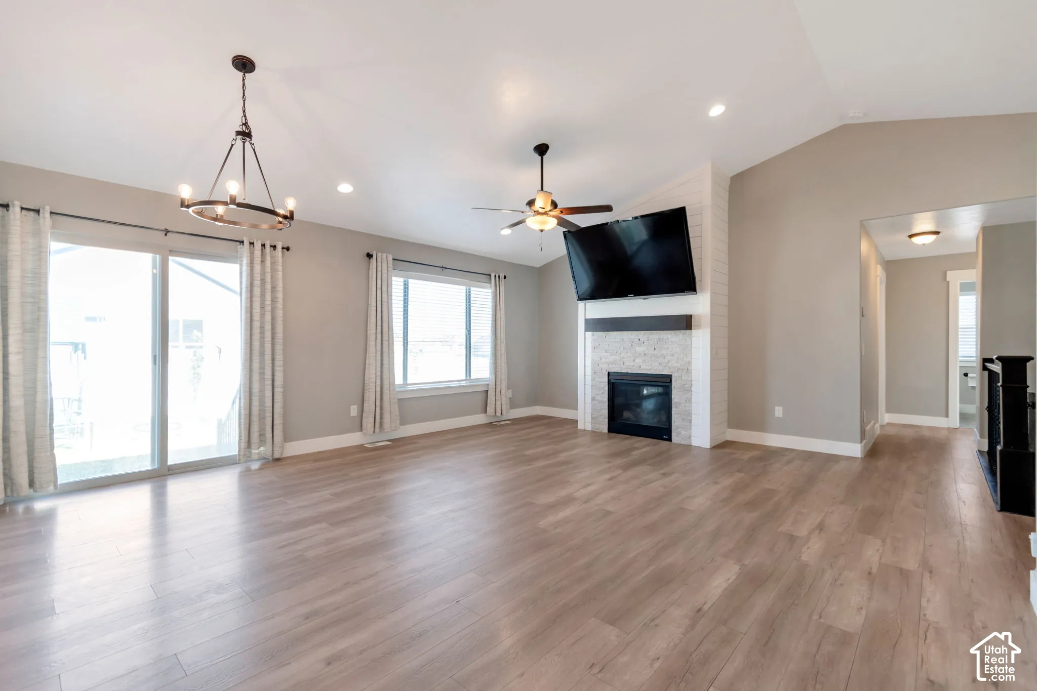 Vaulted ceilings with recessed lighting, wood-finish flooring, a fireplace with a stone surround, and glass sliding doors