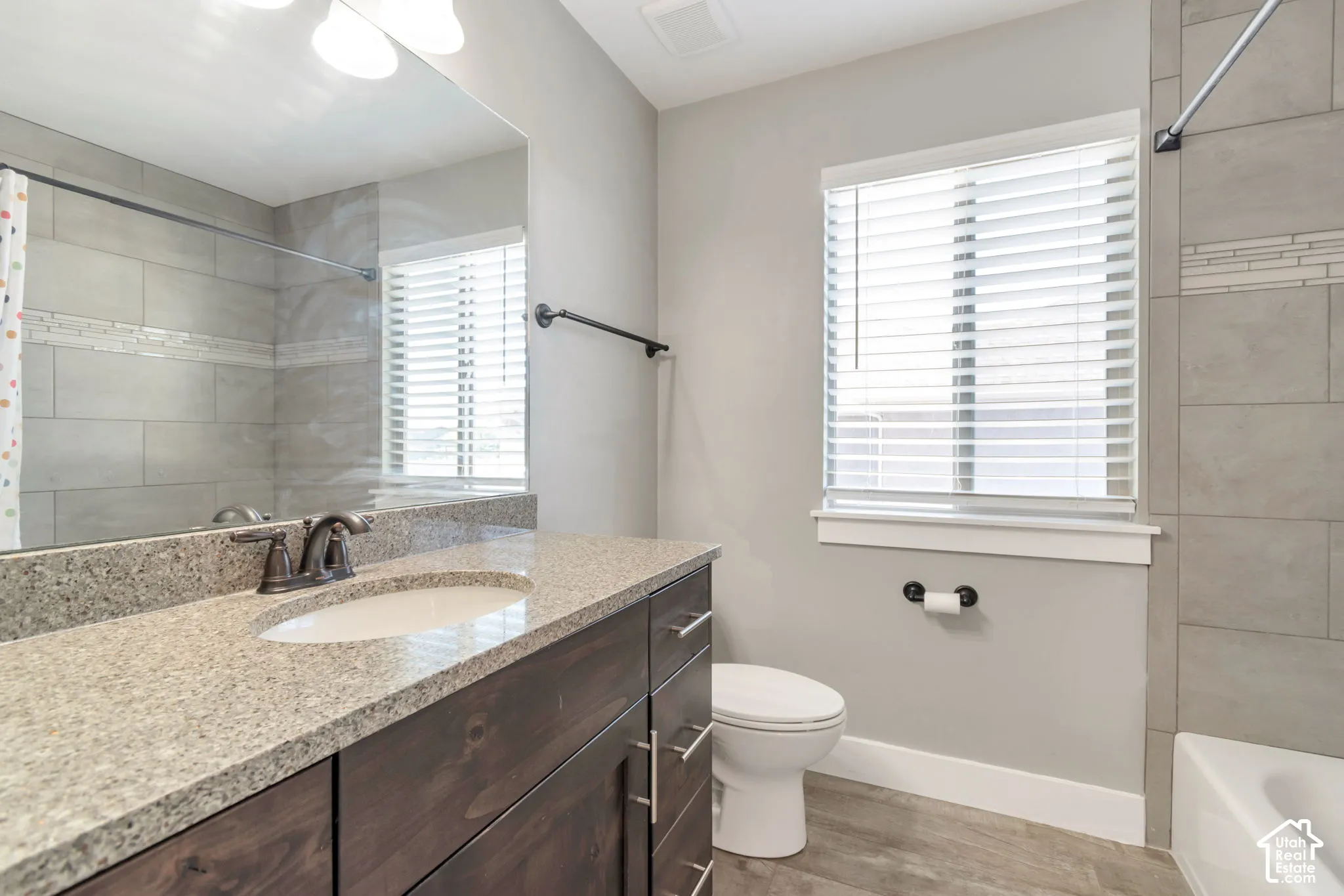 Bathroom featuring a dark wood-finish vanity with a stone countertop, an integrated sink, and a large wall-mounted mirror