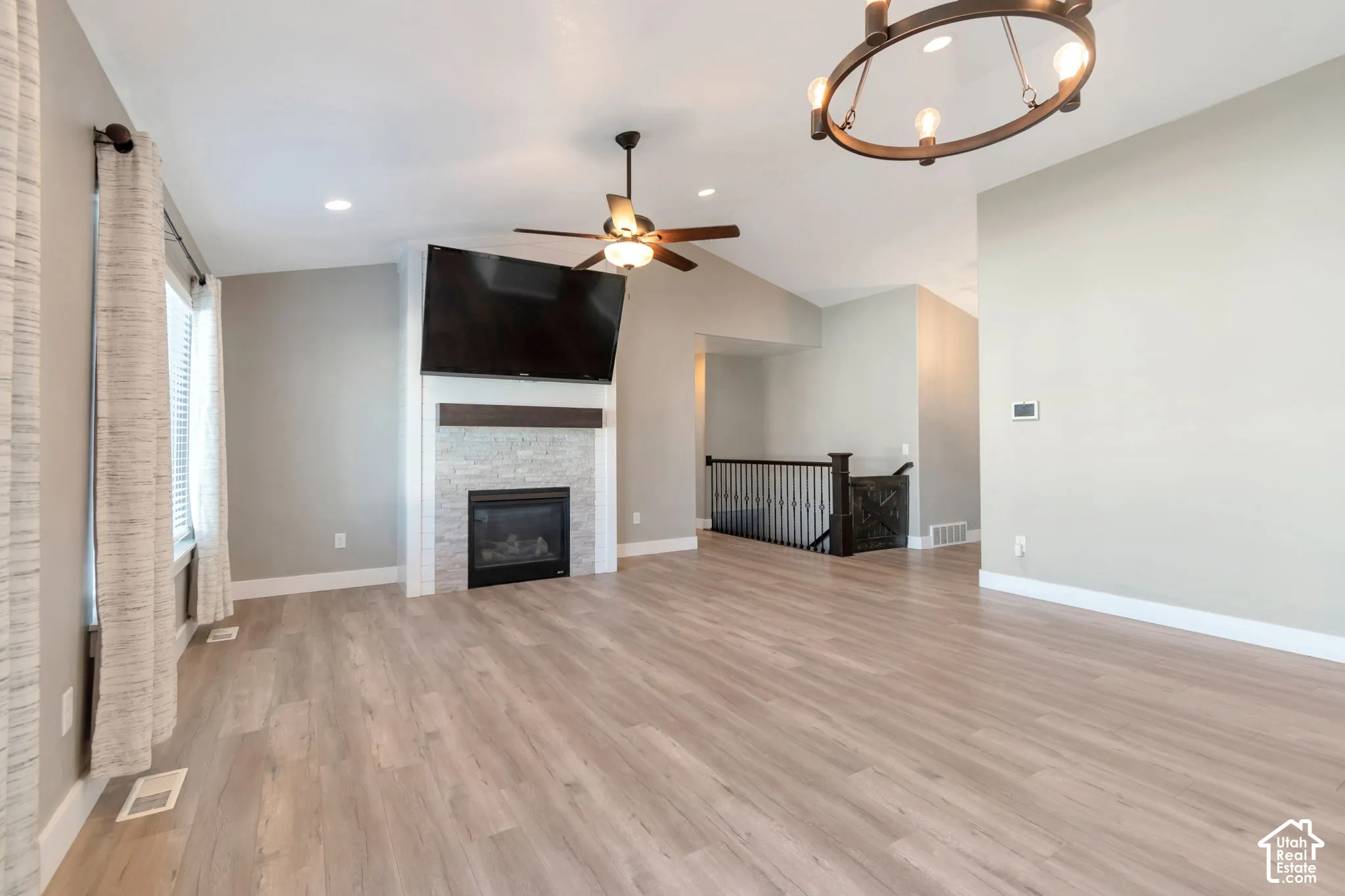 Spacious room featuring wood-finish flooring, a contemporary fireplace with a stone tile surround and wood mantel, a ceiling fan, and an architectural chandelier