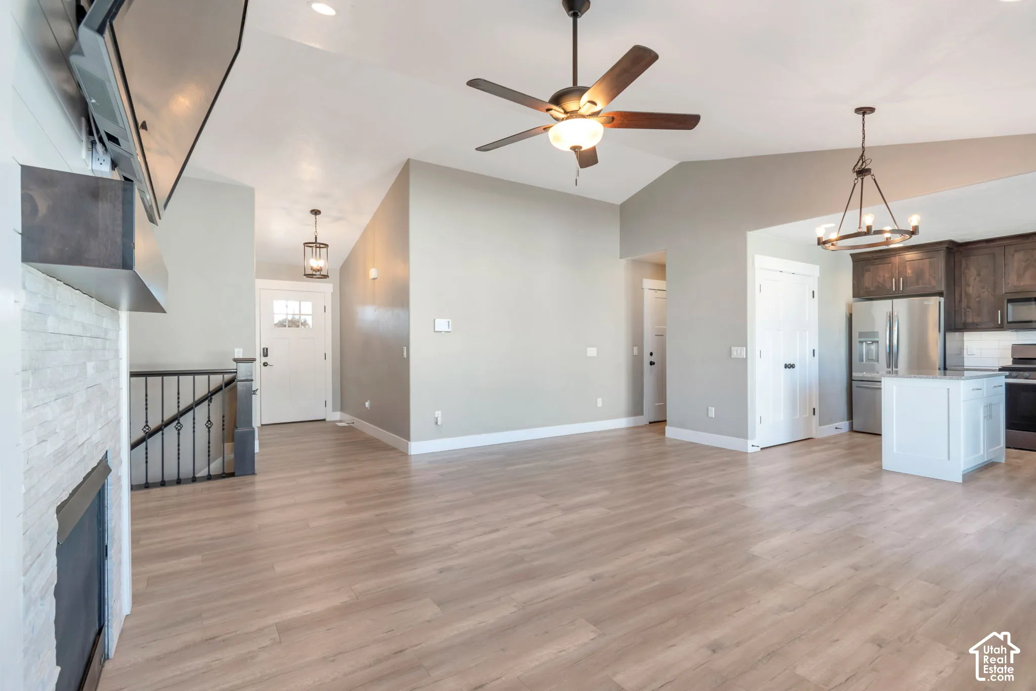 Vaulted ceilings, wood-finish flooring, a stone-clad fireplace, and a kitchen island with pendant lighting