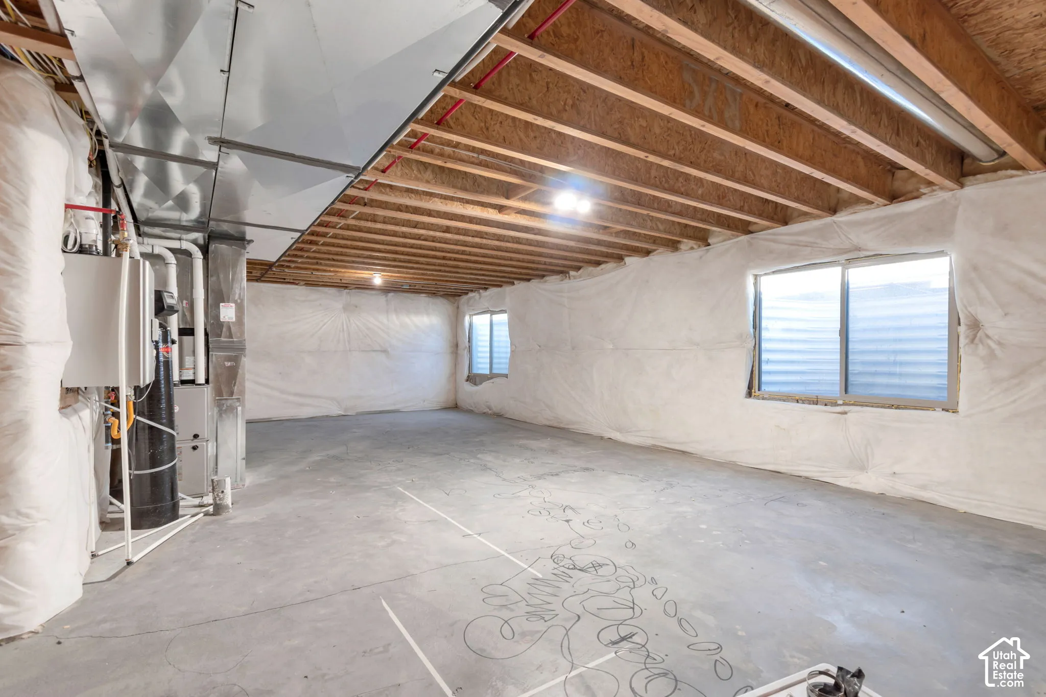 Unfinished basement with concrete flooring, exposed wood ceiling joists, and two windows