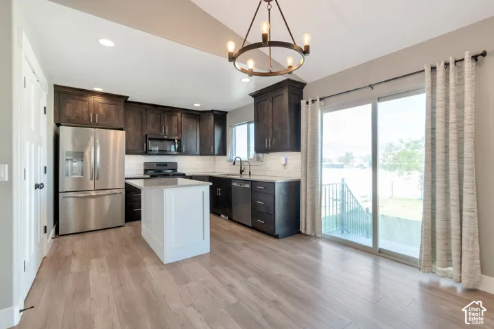 Kitchen featuring wood-finish flooring, dark wood cabinetry, white subway tile backsplash, and a central island with a white base