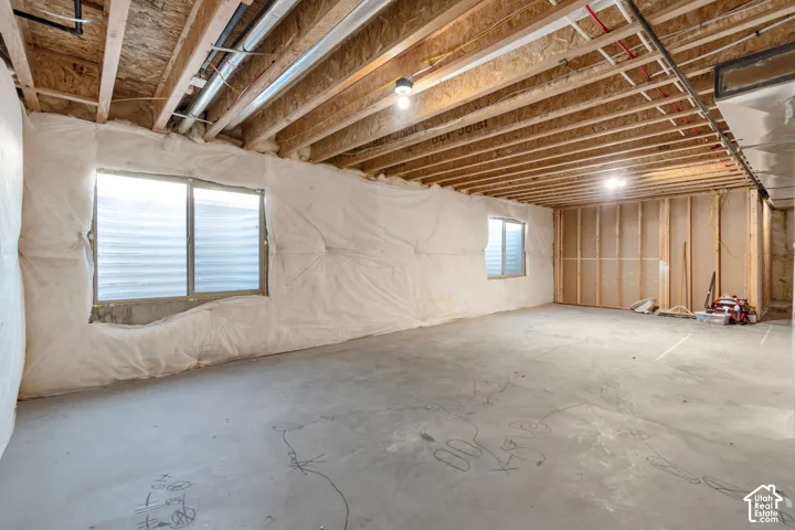 Unfinished basement with exposed ceiling joists, concrete flooring, two basement windows, perimeter insulation, and framed wall sections