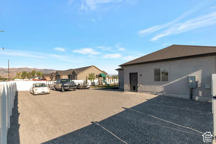 Gravel parking area, white picket fence, stucco exterior, dark roof, and mountain backdrop