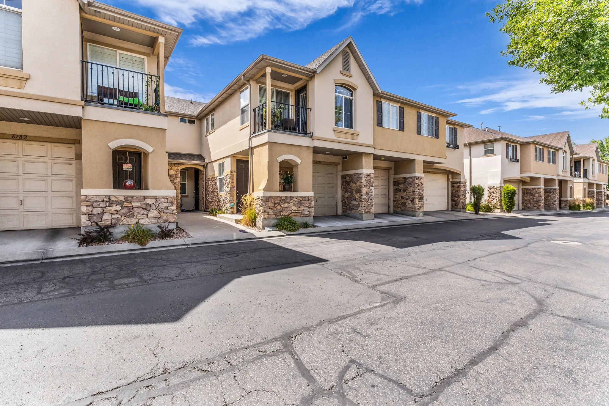 Stucco exterior with stone accents, covered entryways, and upper-level balconies with black railings