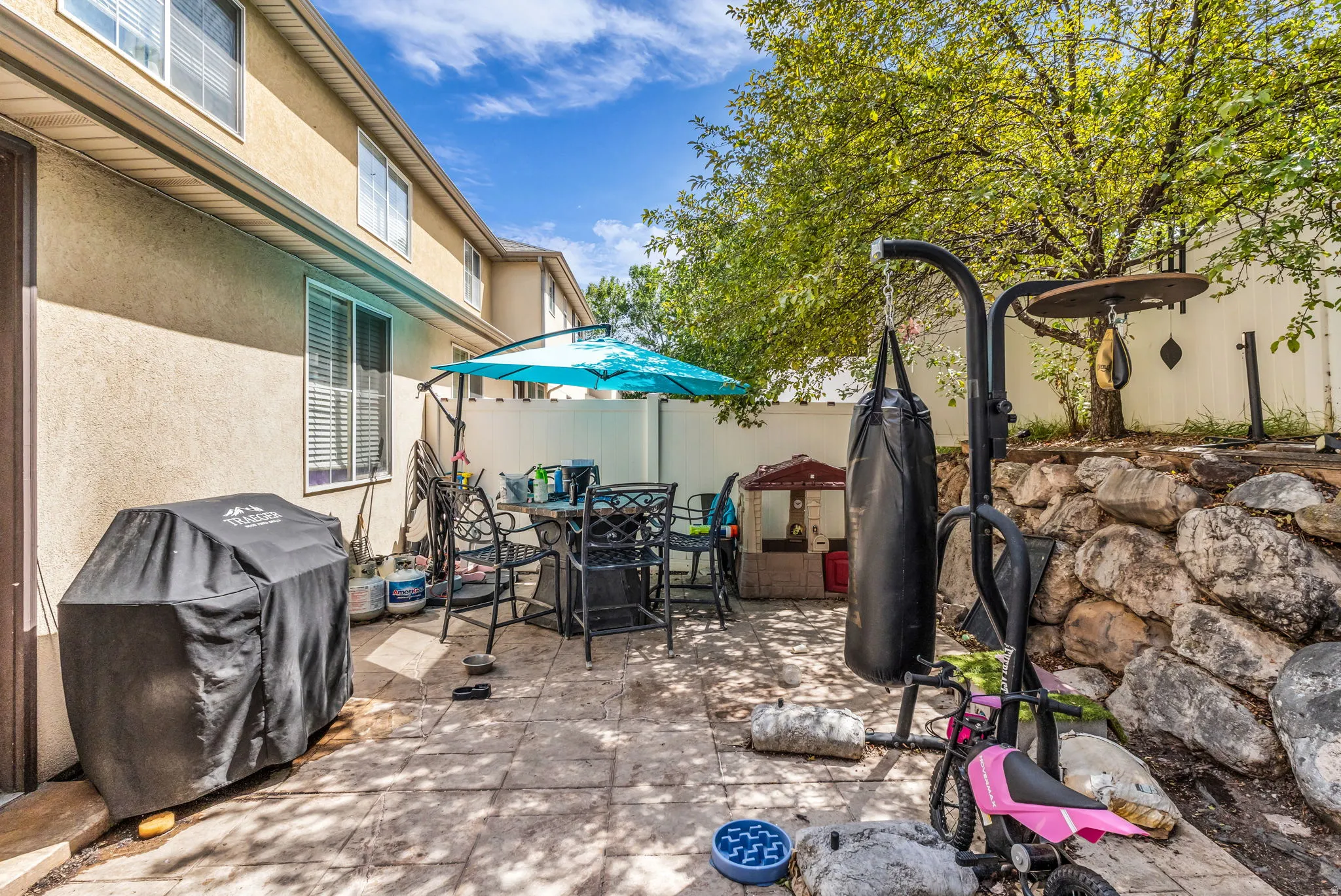 Patio area featuring a paved surface, rock landscaping, privacy fencing, and mature trees