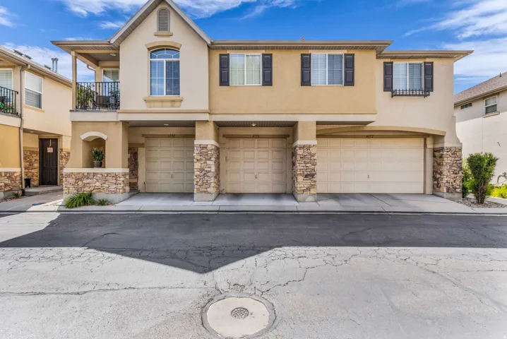Two-story stucco exterior featuring stone accents, a second-story balcony with iron railing, arched windows, and an integrated garage