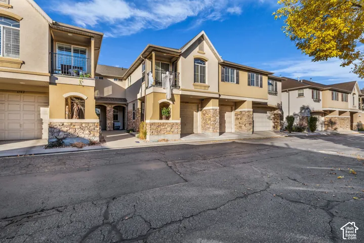 Multi-family exterior featuring a stucco and stone facade, arched entryway detailing, upper-level balconies with metal railings, and multi-car garage access