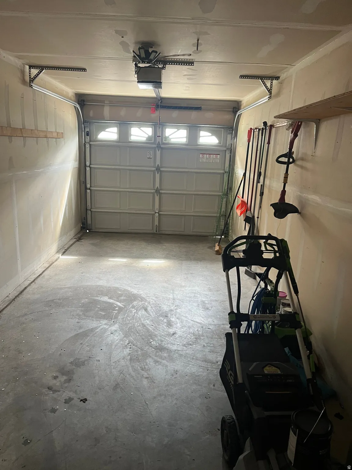 Single-car garage featuring a roll-up door with frosted pane inserts, concrete flooring, exposed overhead door opener, and built-in wall shelving