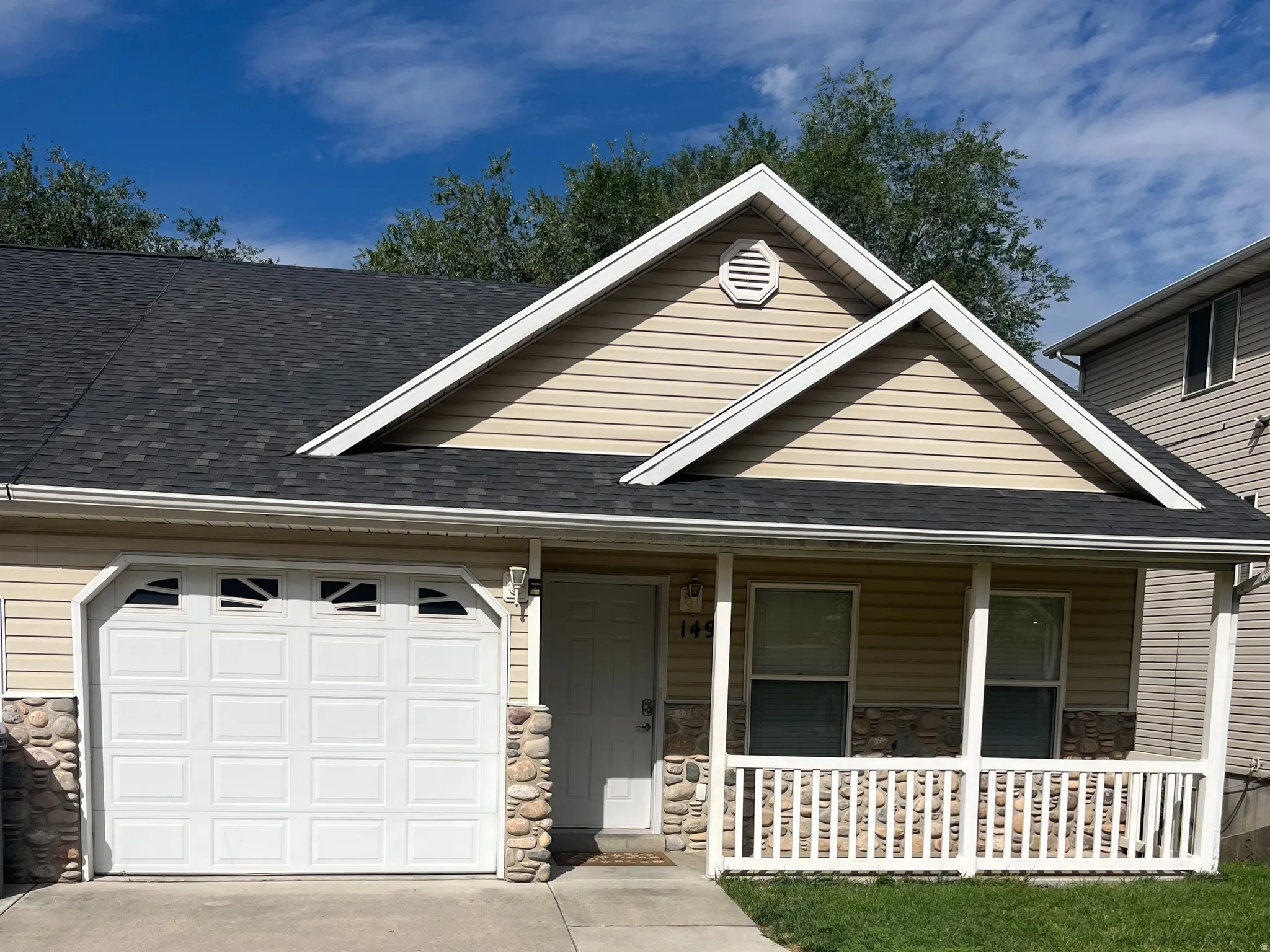 Front exterior featuring beige siding, stone facade accents, white garage door, covered porch with white railing, and a concrete driveway