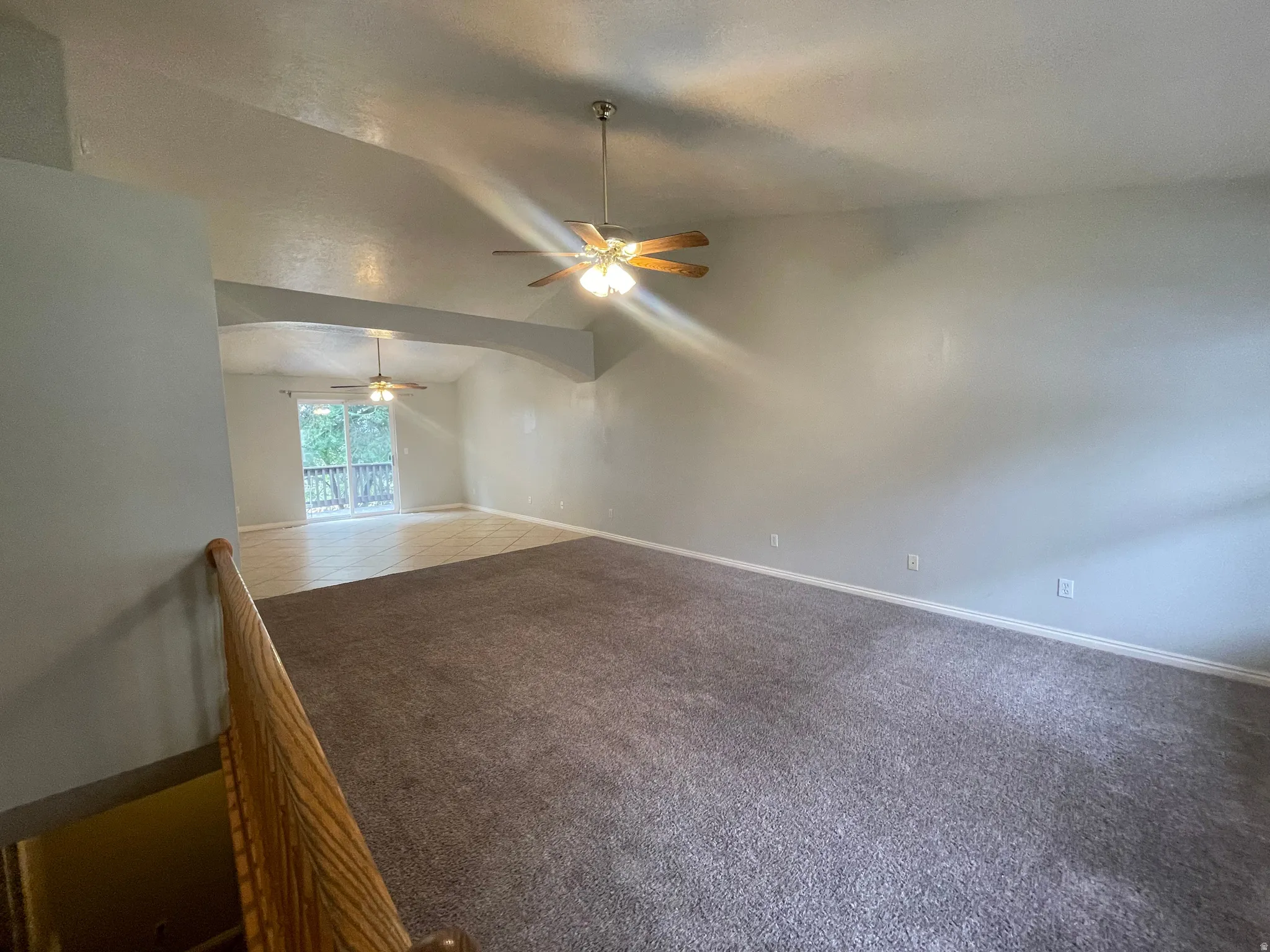 Vaulted ceilings with recessed archway, ceiling fan fixtures, and a glass sliding door leading to an outdoor deck