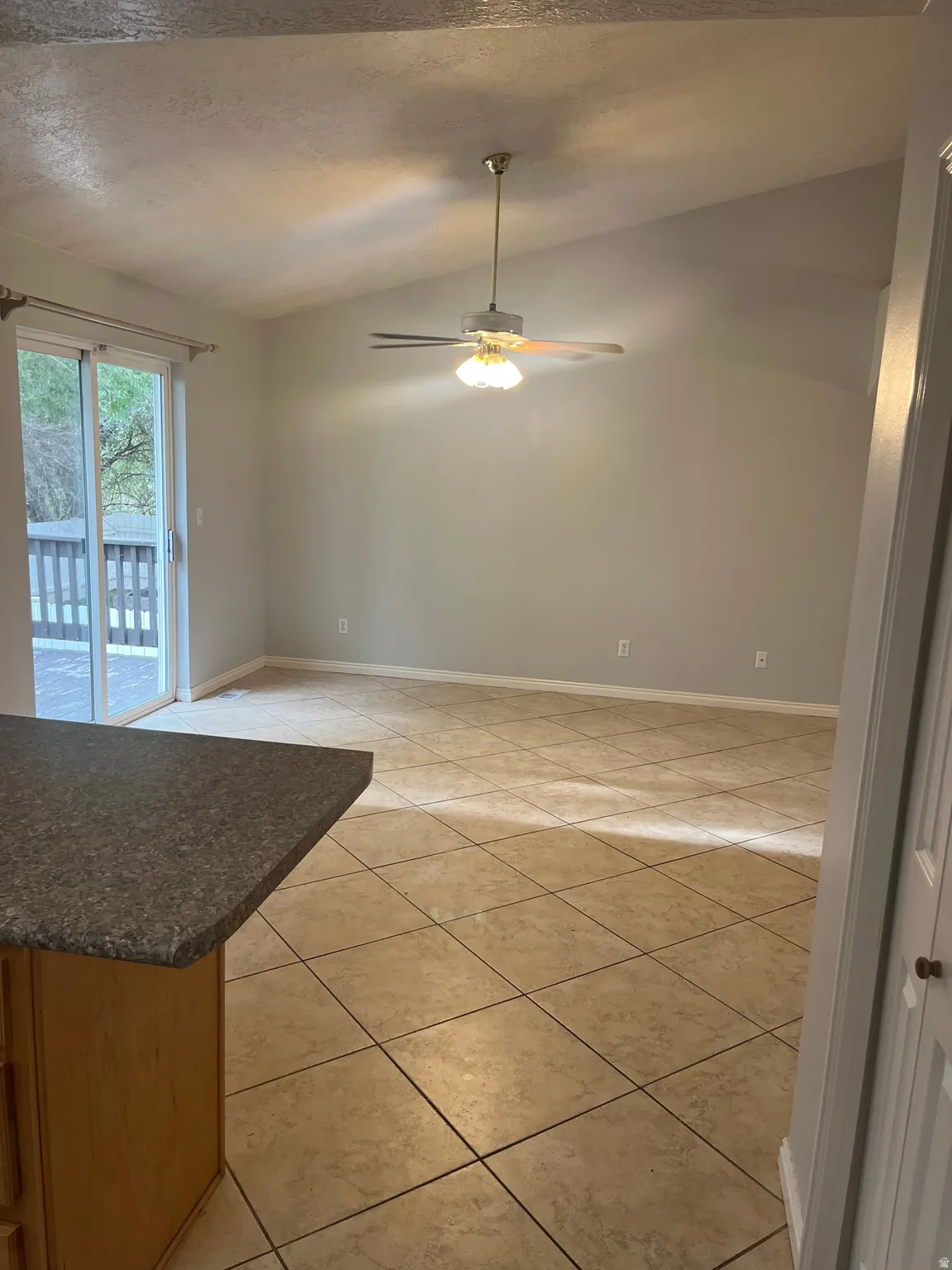 Vaulted ceiling with a ceiling fan, sliding glass door, tile flooring, and a built-in counter