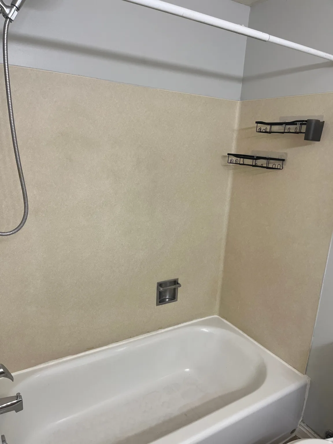 Alcove bathtub with a handheld shower fixture, integrated soap dish, and wall-mounted shelving