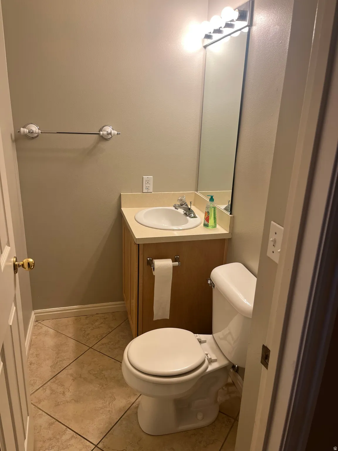 Neutral paint scheme, vanity with integrated sink, chrome faucet, tiled flooring, and a wall-mounted mirror with vanity lighting