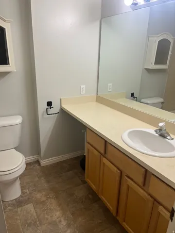 Single vanity with an integrated sink, laminate countertop, light wood-finish cabinetry, and a wall-mounted mirror