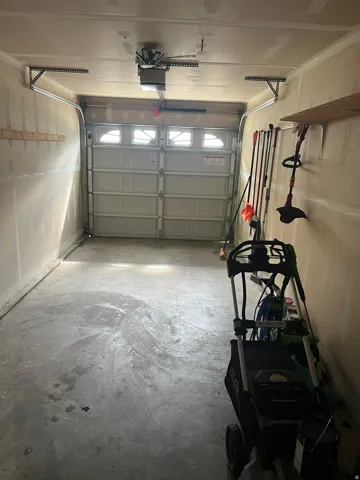 Single-car garage featuring a roll-up door with frosted pane inserts, concrete flooring, exposed overhead door opener, and built-in wall shelving