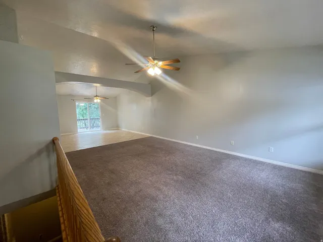 Vaulted ceilings with recessed archway, ceiling fan fixtures, and a glass sliding door leading to an outdoor deck
