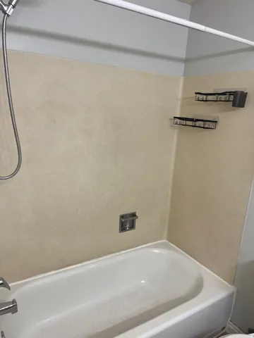 Alcove bathtub with a handheld shower fixture, integrated soap dish, and wall-mounted shelving