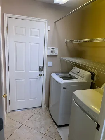 Laundry area featuring tiled flooring, a paneled door, integrated shelving, and a hanging rod
