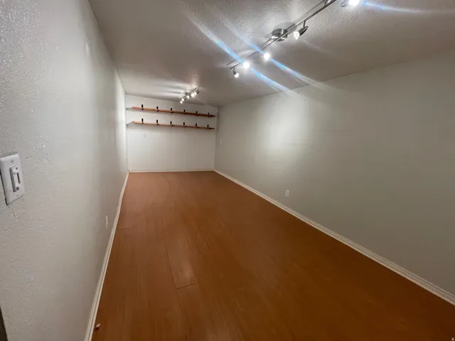Wood-finish flooring with track lighting, white walls, and built-in shelving