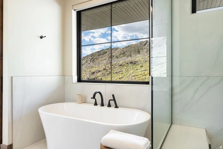 Freestanding soaking tub with black fixtures, large picture window, glass shower enclosure, and white tile surround