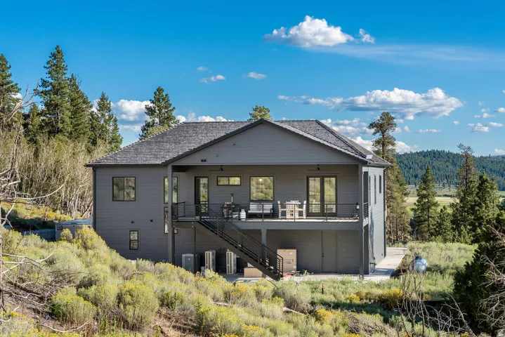 Contemporary exterior with dark gray siding, a prominent second-story deck with black railings, multiple windows for natural light, and a sloped shingle roof