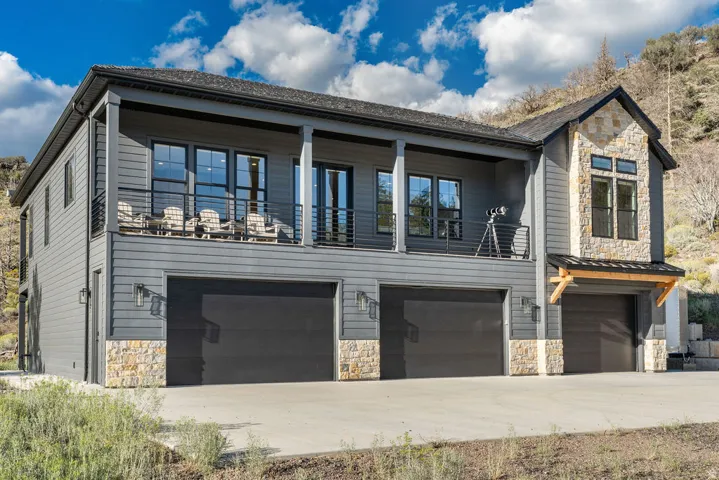 Multi-level exterior with dark horizontal siding, stone accents, multiple garage bays, and an upper-level balcony with metal railing