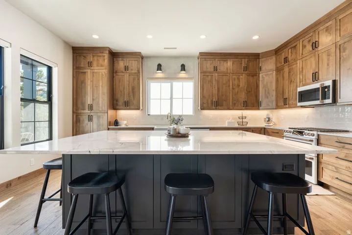 Expansive kitchen island with a stone countertop, abundant wood-finish cabinetry, built-in microwave, and stainless steel range