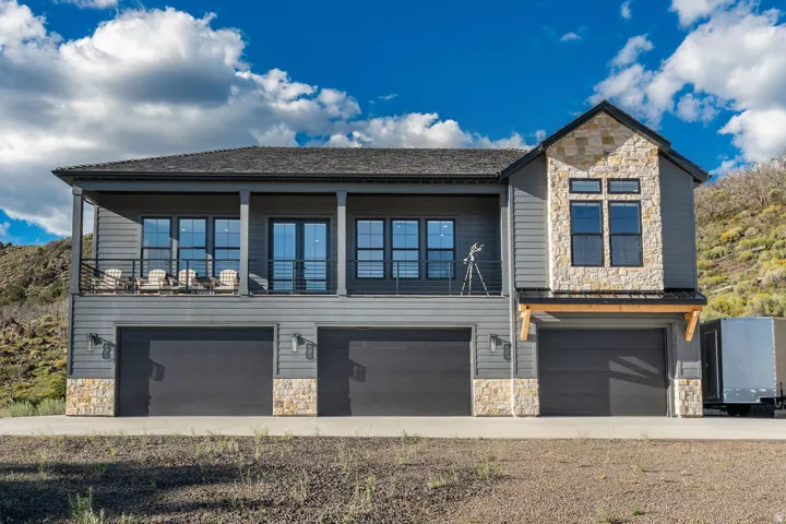 Contemporary exterior featuring a stone facade, multi-pane windows, and a covered balcony with a metal railing