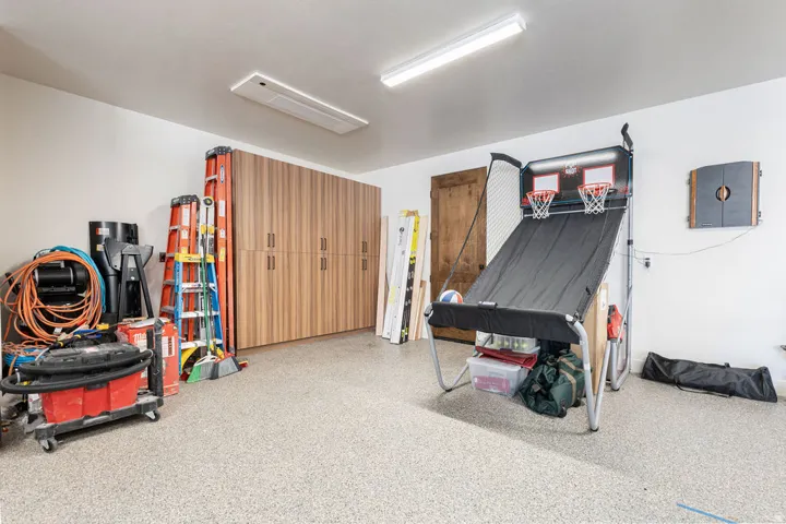 Garage with light-colored epoxy flooring, featuring extensive built-in wood-finish cabinetry, and overhead fluorescent lighting