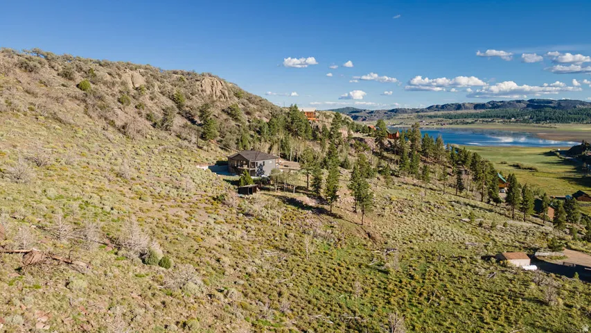 Hillside property with a visible structure, surrounding natural landscape, and distant water feature