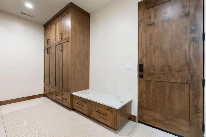 Built-in wood-finish cabinetry, integrated bench with a stone surface, wood-finish door, and recessed lighting