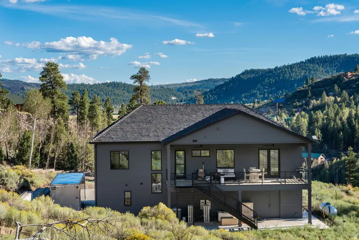 Gray exterior with a dark shingled roof, featuring a raised deck with metal railings and exterior stairs