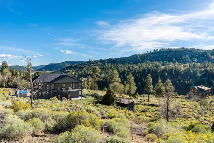 Contemporary-style residence with a dark exterior, multi-level decking, and an outdoor swimming pool, set against a backdrop of forested hills