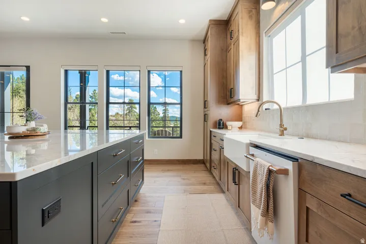 Expansive kitchen featuring a large central island with storage, natural wood-finish flooring, light-toned countertops, shaker-style cabinetry, and a farmhouse sink with a gooseneck faucet