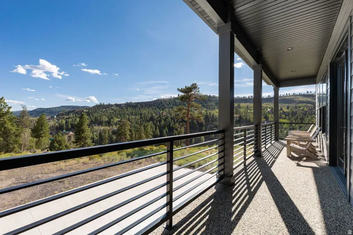 Covered balcony featuring a black metal horizontal railing system, exposed aggregate flooring, and recessed lighting