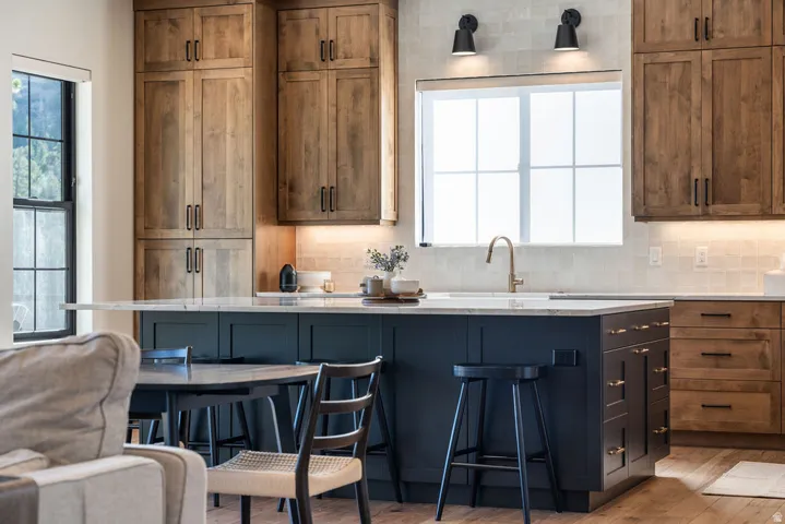 Custom cabinetry with matte black hardware, large kitchen island with integrated seating, undermount sink with a brass-finish faucet, subway tile backsplash, and wood-finish flooring