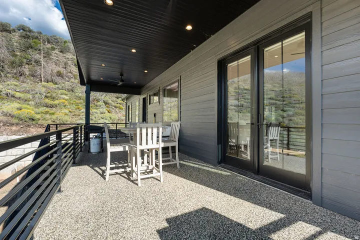 Covered patio with exposed aggregate flooring, black metal railing, and recessed lighting